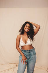 Curvy fashion model wearing bra and jeans standing against white background  stock photo