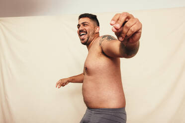 Dancing in grey underwear. Happy shirtless man dancing cheerfully while standing against a studio background. Body positive and self-confident man celebrating his natural body. - JLPSF12250