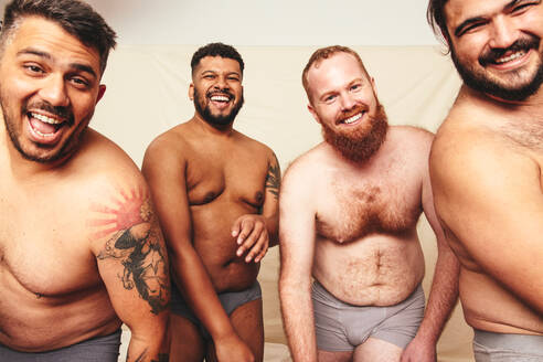 Having fun while shirtless. Three happy men smiling at the camera while wearing underwear in a studio. Body positive and self-confident men celebrating their natural bodies. - JLPSF12256