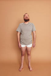 Studio portrait of a happy man standing alone. Body positive young man smiling cheerfully while standing against a studio background. Self-confident young man feeling comfortable in his natural body. - JLPSF12277