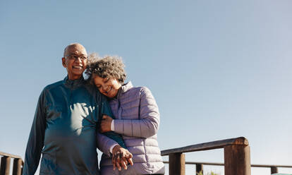 Fröhliches älteres Paar, das lächelnd und händchenhaltend einen Spaziergang an der Strandpromenade unternimmt. Romantisches älteres Paar, das nach seiner Pensionierung einen entspannenden Urlaub am Meer genießt. - JLPSF12299