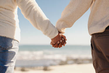 Rückenansicht eines reifen Paares, das auf einem hölzernen Steg am Strand steht und sich an den Händen hält. Romantisches älteres Paar, das nach seiner Pensionierung einen erfrischenden Urlaub am Meer verbringt. - JLPSF12303
