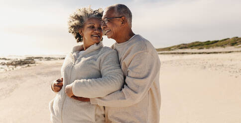 Reife Romantik am Strand. Glückliches älteres Paar, das lächelt und sich umarmt, während es am Strand steht. Zärtliches älteres Paar, das seinen Ruhestand zusammen genießt. - JLPSF12313