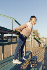Lächelndes Mädchen mit Pullover auf einer Treppe am Strand - JBUF00078