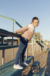 Smiling girl wearing sweater on staircase at beach - JBUF00078