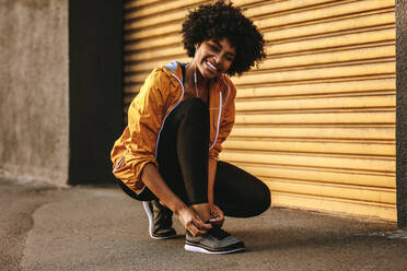 Smiling african woman in fitness wear tying her shoelace. Fitness woman tightening her shoes during workout. - JLPSF12325