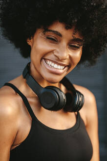Eine Läuferin lächelt nach einem morgendlichen Lauf. Eine Frau in Fitnesskleidung mit Kopfhörern um den Hals. - JLPSF12337