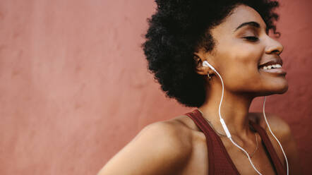 Close up of woman athlete with earphones against brown background. Woman listening to music after workout. - JLPSF12359