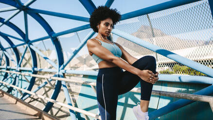 Fitte junge Frau dehnt ihr Bein nach einem Lauf in der Stadt. Afrikanische Frau in Sportkleidung bereitet sich auf ein Lauftraining vor. - JLPSF12374