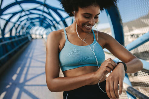 Fitte Läuferin, die ihre Leistung mit einer Smartwatch überwacht. Afrikanische Frau, die vor dem Laufen eine Fitness-App auf ihrer Smartwatch einstellt. - JLPSF12375