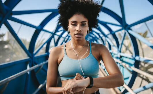 Junge Fitness-Frau mit Smartwatch, die in die Kamera schaut. Sportlerin, die den Puls auf der Smartwatch-Fitness-App überprüft. - JLPSF12376