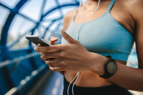 Ausgeschnittenes Bild einer Frau in Sportkleidung, die ein Mobiltelefon benutzt, mit Fokus auf Hände und Smartphone. - JLPSF12382