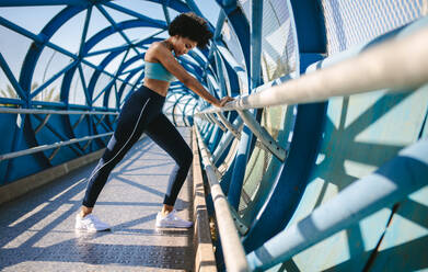 Fitness Frau tun Stretching mit der Unterstützung der Brücke Geländer. Weibliche Athleten tun Stretching-Übungen. - JLPSF12384