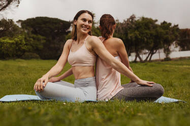 Zwei Fitness-Frauen machen Yoga in einem Park. Frauen, die zusammen in entgegengesetzter Richtung sitzend Drehübungen machen. - JLPSF12433