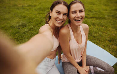 Nahaufnahme von zwei Fitness-Frauen, die in einem Park sitzen und ein Selfie machen. Freunde haben Spaß nach dem Training und machen ein Selfie. - JLPSF12439