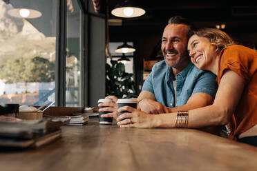 Glückliches Paar, das sich in einem Café bei einer Tasse Kaffee entspannt. Lächelnder Mann und lächelnde Frau sitzen in einem Café und schauen gemeinsam aus dem Fenster. - JLPSF12444