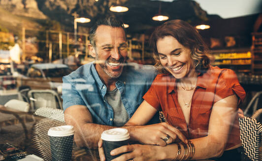 Ein Paar sitzt in einem Café und lächelt. Ein Paar bei einem Date in einem örtlichen Café. - JLPSF12446