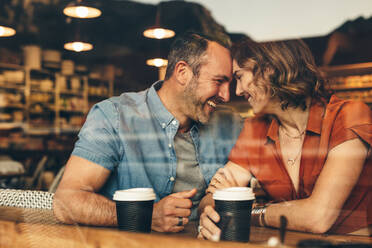 Verliebtes Paar bei einer Verabredung im Café. Das Paar sitzt im Café, berührt die Stirn und lächelt. - JLPSF12447
