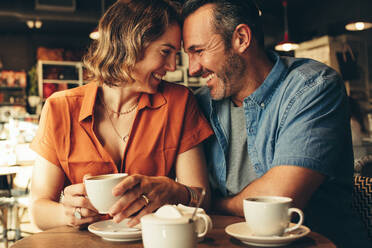 Verliebtes Paar sitzt im Café, berührt die Stirne und lächelt. Schönes verliebtes Paar bei einem Kaffee-Date. - JLPSF12455