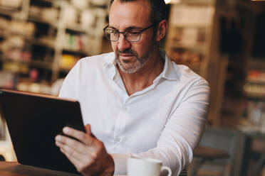 Geschäftsmann, der in einem Café an seinem digitalen Tablet arbeitet. Mann, der seinen Tisch-PC im Café benutzt. - JLPSF12457