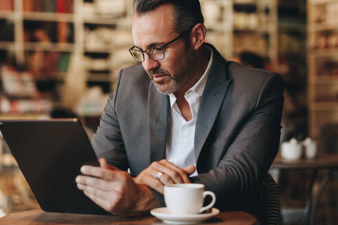 Geschäftsmann liest eine E-Mail auf seinem digitalen Tablet in einem Café. Geschäftsmann in einem Café arbeitet an einem digitalen Tablet. - JLPSF12459