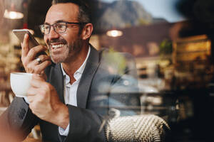 Businessman making a phone call from a coffee shop. Business professional having coffee and talking on speaker phone. - JLPSF12462