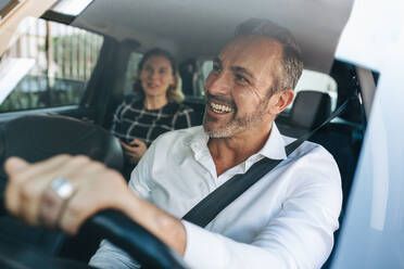 Taxi driver talking to a female passenger sitting in backseat. Businesswoman using taxi ride to go to work. - JLPSF12465