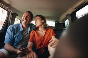Verliebtes Pärchen auf dem Rücksitz eines Taxis. Lächelnder Mann und lächelnde Frau beim Aussteigen in einem Taxi. - JLPSF12469