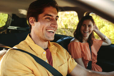 Cheerful young couple on a roadtrip. Smiling man driving the car with women sitting on passenger seat. - JLPSF12489