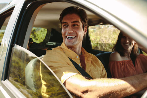 Ein Mann fährt Auto und schaut aus dem Fenster, während eine Frau auf dem Beifahrersitz sitzt und lächelt. Ein Paar macht einen Ausflug in den Urlaub. - JLPSF12490