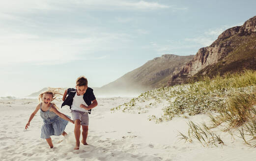 Two adorable children running together at the beach. Brother and sister playing on the beach. - JLPSF12500