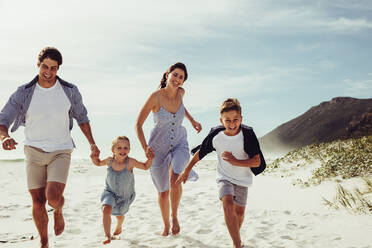 Happy young family of four running together on the beach. Parents with kids running along the beach. - JLPSF12501