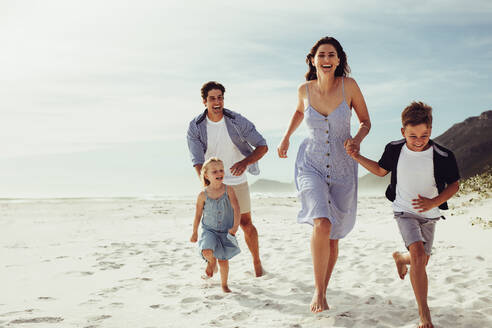 Eine vierköpfige Familie, die gemeinsam am Meer läuft. Ein Paar mit Kindern, das am Strand entlang läuft. - JLPSF12502
