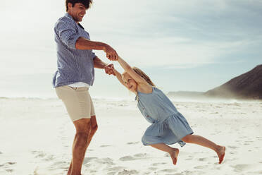 Happy father swinging his daughter around on the beach. Man playing with his daughter on beach vacation. - JLPSF12503