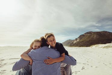 Rear view of a man embracing his kids on the beach. Father with his children on vacation. - JLPSF12507