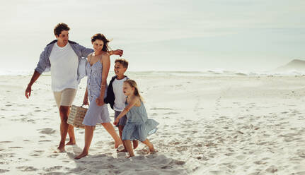 Glückliche Familie, die mit einem Picknickkorb am Strand spazieren geht. Vierköpfige Familie im Strandurlaub. - JLPSF12510