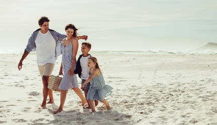 Happy family walking along beach with picnic basket. Family of four on beach vacation. - JLPSF12510