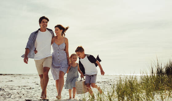 Familie, die am Strand spazieren geht, mit Kindern, die einen Picknickkorb tragen. Schöne Familie am Strand an einem Sommerwochenende. - JLPSF12514