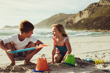 Zwei Kinder spielen mit Sand am Strand. Kleiner Junge und Mädchen bauen eine Sandburg am Meer in den Sommerferien. - JLPSF12520