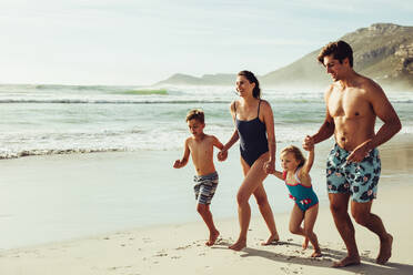 Fröhliche Familie, die am Strand läuft. Glückliche Mutter und Vater mit zwei Kindern, die sich im Sommerurlaub amüsieren. - JLPSF12523