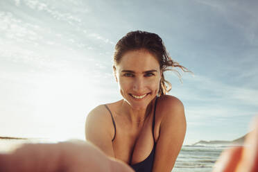 Frau schaut in die Kamera und macht ein Selfie. Blickwinkel einer Frau in Badekleidung, die in die Kamera schaut und den Sommerurlaub am Strand genießt. - JLPSF12529