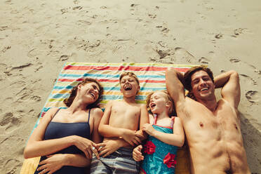 Draufsicht auf eine Familie, die am Strand liegt. Glückliche Mutter und Vater mit zwei Kindern, die sich im Sommerurlaub am Strand entspannen. - JLPSF12532