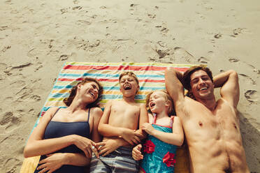 Top view of family lying on the beach. Happy mother and father with two children relaxing on beach on summer holiday. - JLPSF12532