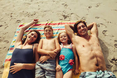 Familie liegt auf der Decke am Strand, schaut in die Kamera und lächelt. Glückliche Familie hat Spaß am Strand. - JLPSF12533