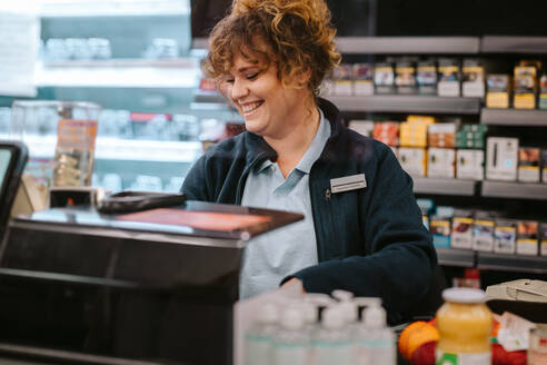 Glückliche weibliche Kassiererin in einem Supermarkt. Frau arbeitet an der Kasse eines örtlichen Lebensmittelgeschäfts. - JLPSF12536