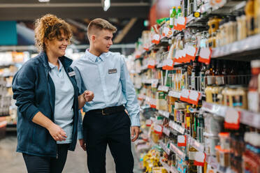 Weibliche Führungskraft hilft einem neuen männlichen Auszubildenden in einem Lebensmittelgeschäft. Ein Mann, der in den Ferien arbeitet, erhält Hilfe von der Führungskraft im Supermarkt. - JLPSF12539