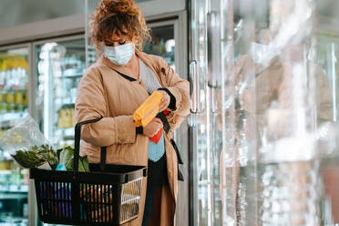 Frau mit Gesichtsmaske beim Einkaufen von Lebensmitteln im Supermarkt. Weibliche Kundin mit Gesichtsmaske beim Einkaufen im Supermarkt. - JLPSF12544