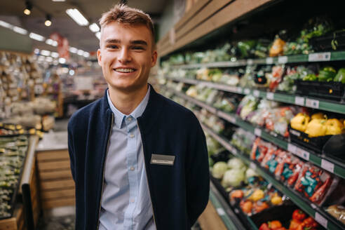 Porträt eines jungen Supermarktangestellten, der in die Kamera lächelt. Mann bei einem Ferienjob in einem Supermarkt. - JLPSF12548