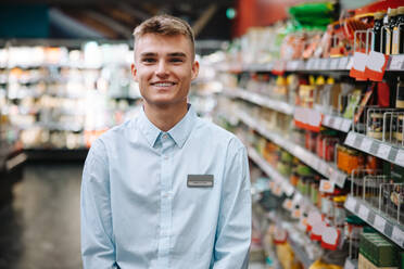Porträt eines jungen Studenten, der in einem Lebensmittelladen arbeitet. Ein Mann bei einem Ferienjob in einem modernen Supermarkt. - JLPSF12561