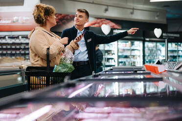 Supermarktangestellte, die einem Kunden den Weg zu einem Gang weist. Ein Kunde bittet um Hilfe für einen Auszubildenden. - JLPSF12565